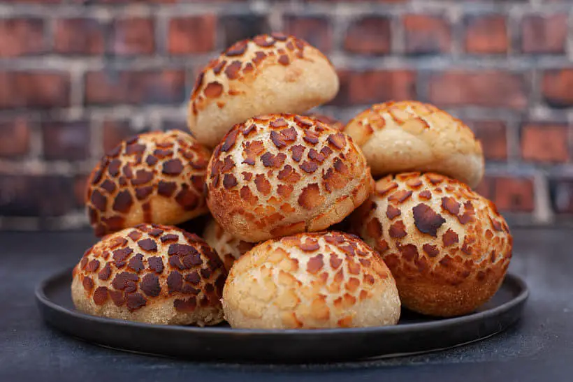 Sourdough tiger bread rolls on a gray plate in front of a brick wall