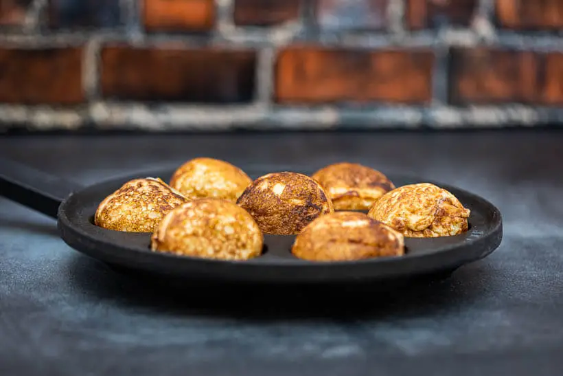 Pan full of sourdough æbleskiver in front of a brick wall