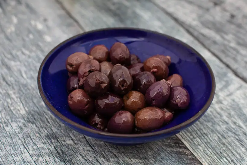 Kalamata olives in a blue bowl on a wooden floor