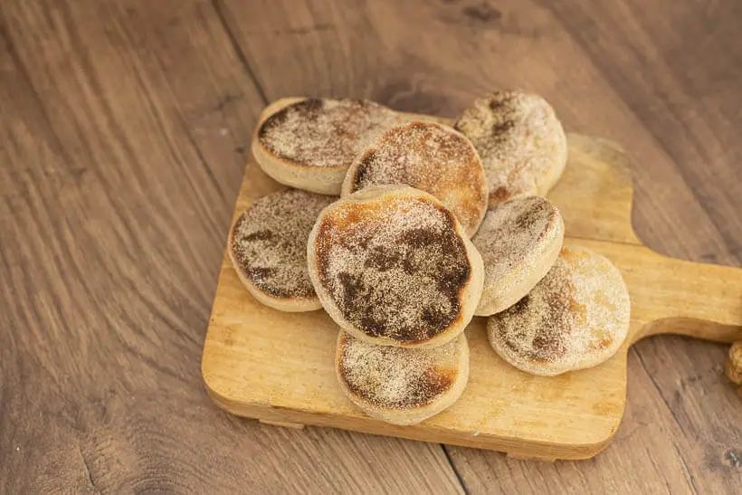 A heap of English muffins on a wooden board