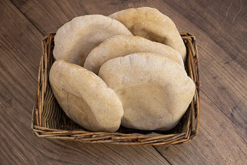 Sourdough pita bread in a basket on a wooden floor made with this recipe