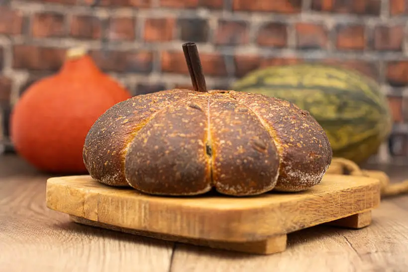 sourdough pumpkin bread on a board in front of real pumkins