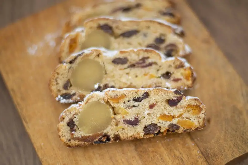 Slices of sourdough stollen with rum-soaked dried fruit and a roll of marzipan on a wooden board
