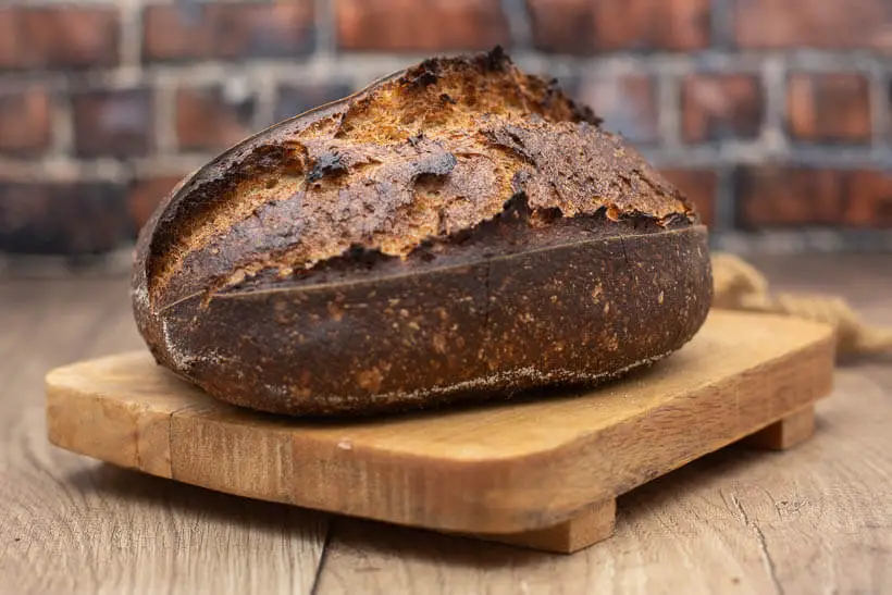 A sourdough bread on a wooden board in front of a brick wall