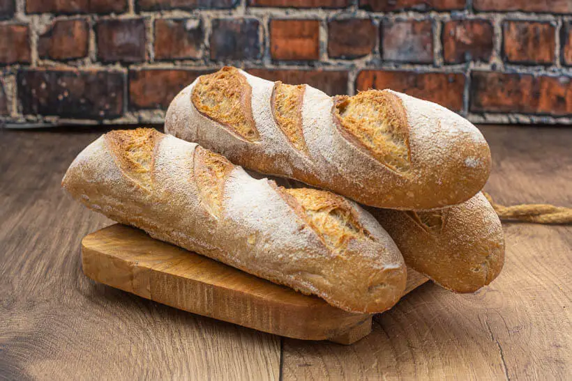Sourdough baguettes on a wooden board in front of a brick wall