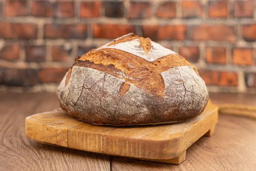 Crusty, yeasted artisan bread on a board in front of a brick wall