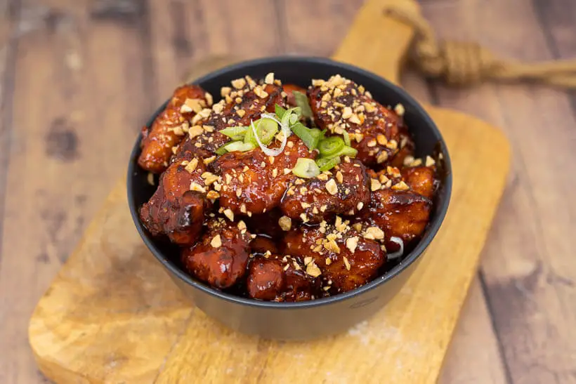 korean fried chicken in a bowl topped peanuts and scallions