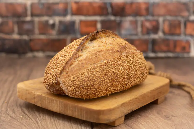 sesame sourdough bread on a board in front of a brick wall