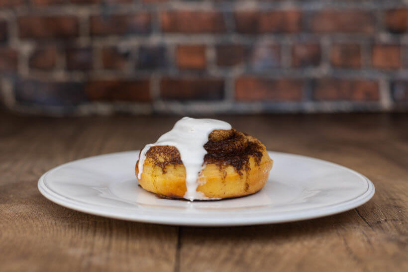 a cinnamon roll on a plate in front of a brick wall