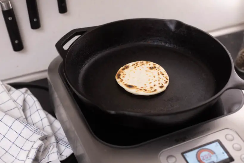 a homemade tortilla being prepared on a cast iron skillet